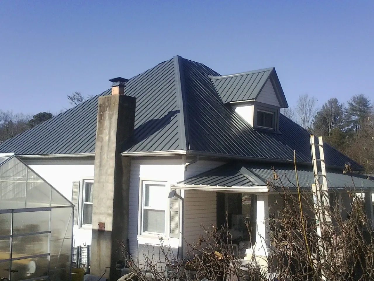 Dark blue standing seam metal roof on a white farmhouse with dormer — Slate & Tile Roof Repair by Roofing Brothers in Rexford