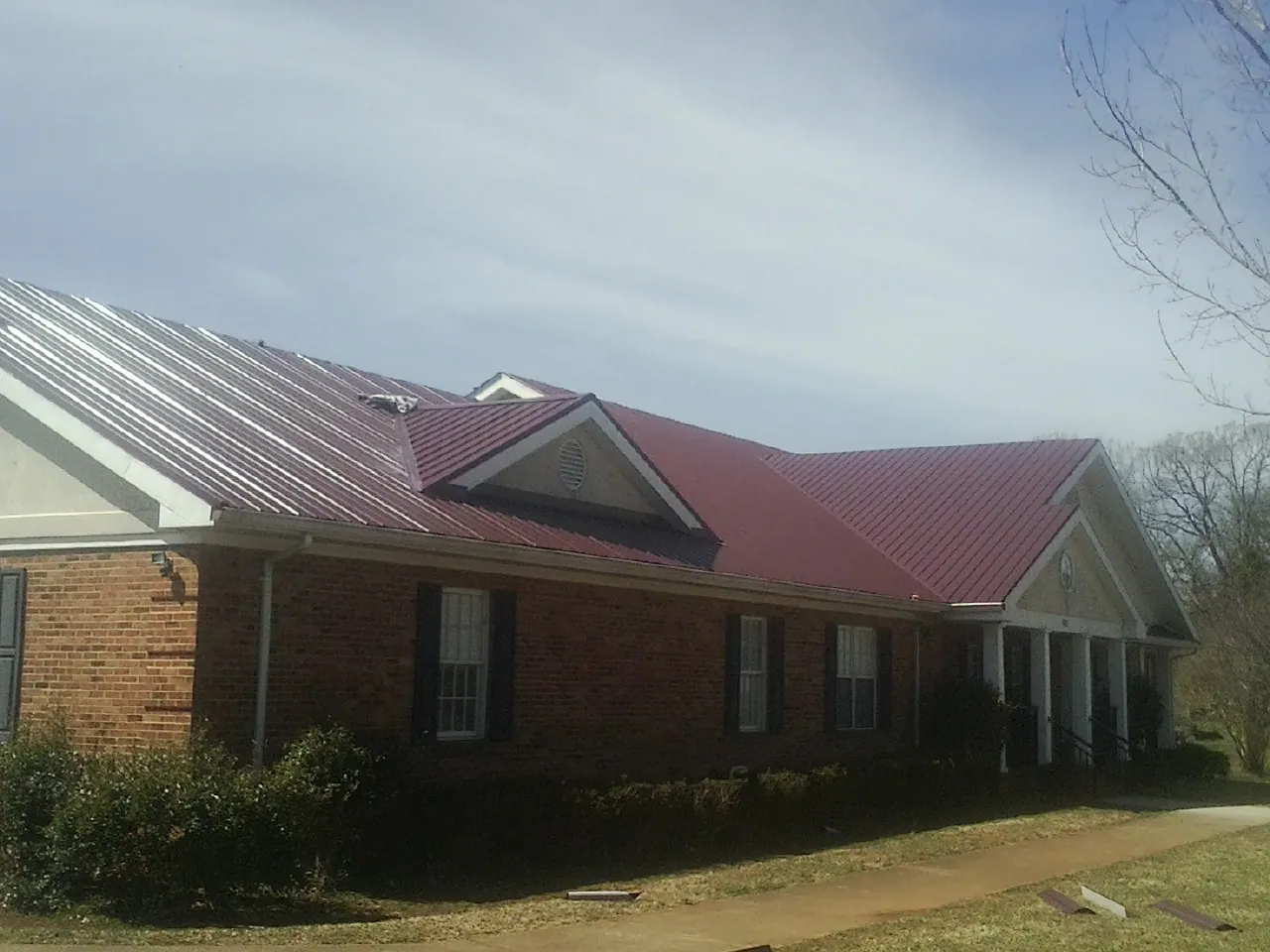 Red metal roof with gabled entries on a long brick building, from a Hail Damage Roof Repair job in Rexford