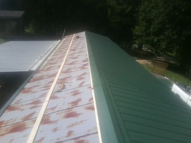 Old rusted panels beside newly installed green metal roofing — Wind Damage Roof Repair by Roofing Brothers in Rexford