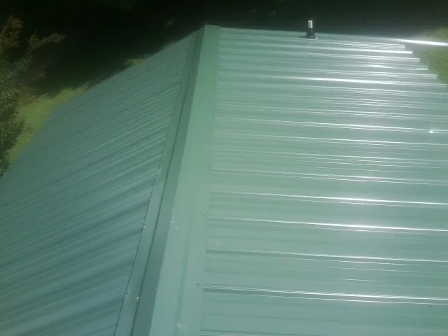 New green metal panels meeting at the ridge of a roof — Flat Roof Repair work by our crew in Rexford