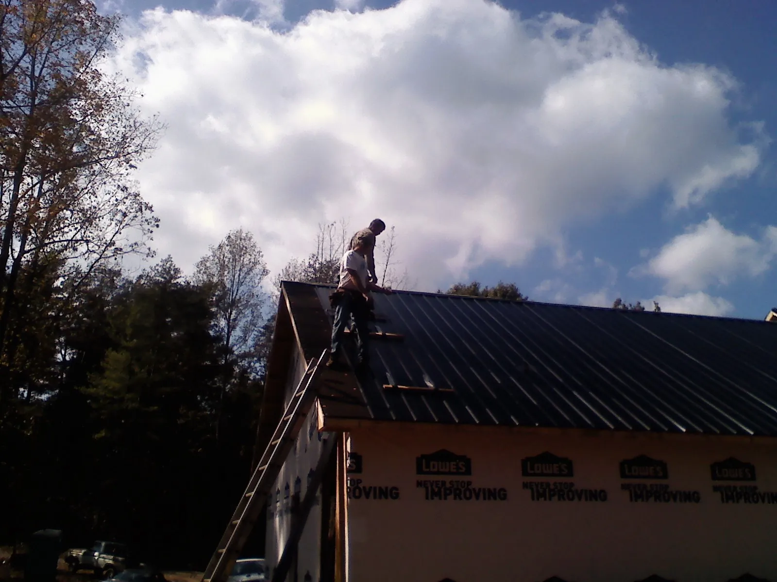 Roofer fastening dark metal panels high against a cloudy sky, from a Roof Inspection job in Rexford