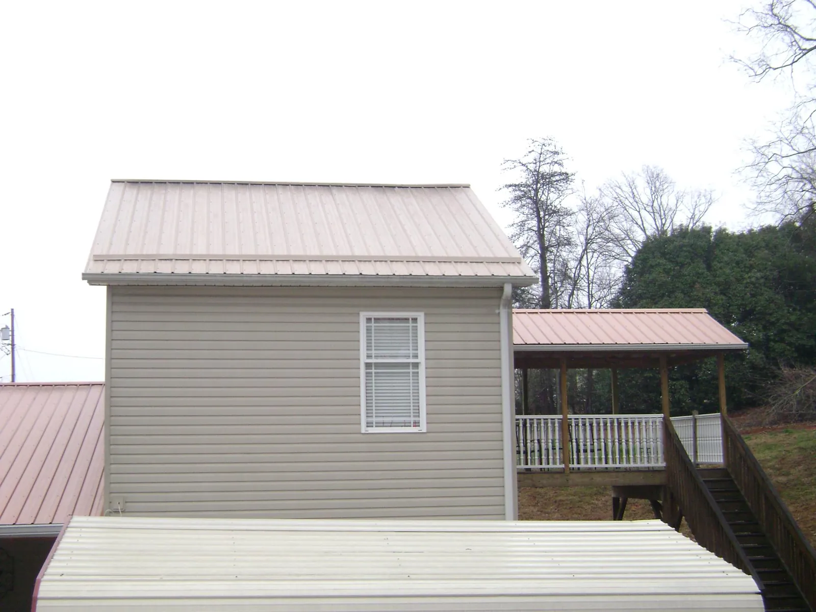 Tan metal roofs on a two story addition and attached porch, from a Roof Replacement job in Rexford